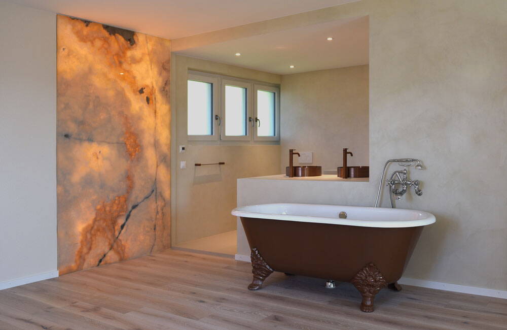 Durch Wandöffnung erweitertes Badezimmer, hinterleuchtete Marmorwand, freistehende Badewanne mit Füssen