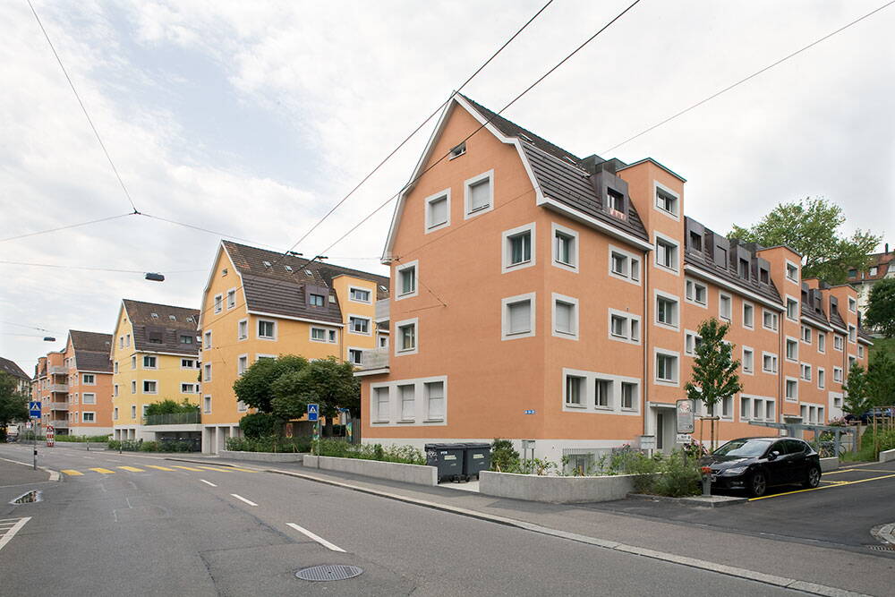 Aussenansicht von Strasse her auf vier grosse Mehrfamilienhäuser mit Giebeldächern der Überbauung Steinstrasse. Energetisch Sanierte Gebäudehülle in Orangetönen.