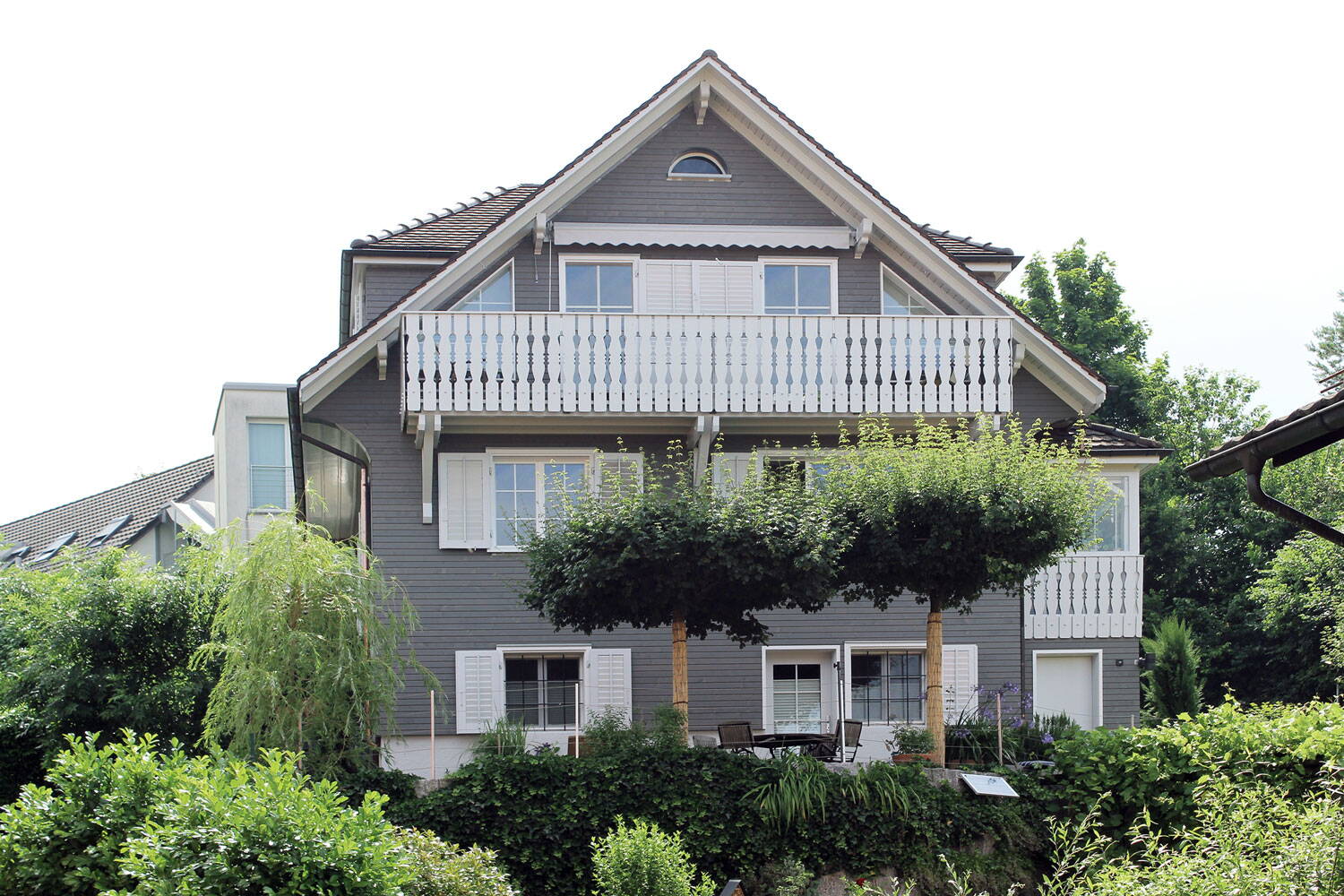 Aussenansicht Einfamilienhaus, Stäfa mit neuer grauer Holzfassade und weissen Balkonverkleidungen sowie Fensterläden. Giebeldach. 