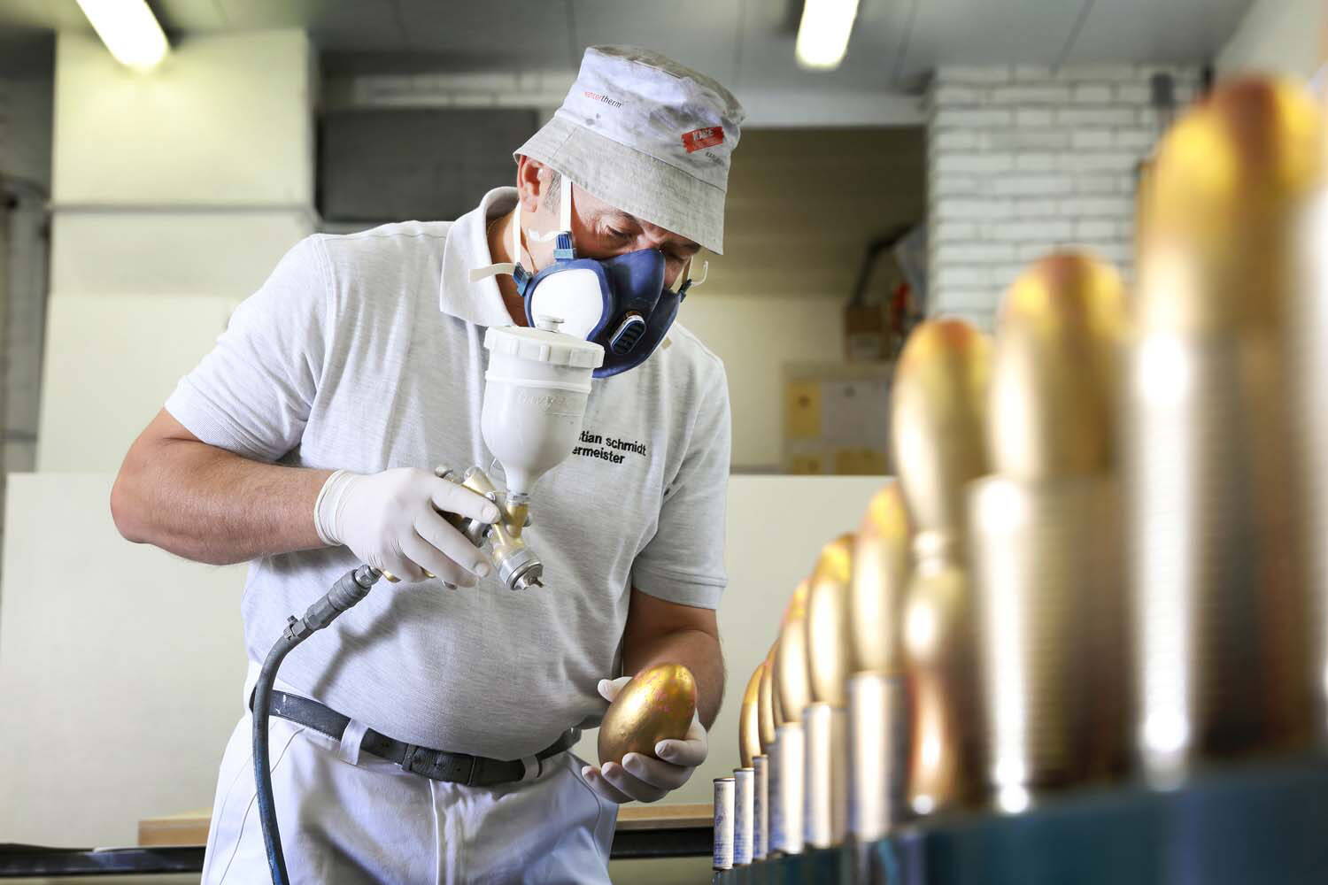 Ein Mann mit Schutzmaske besprüht Holzelemente mit goldenem Lack.