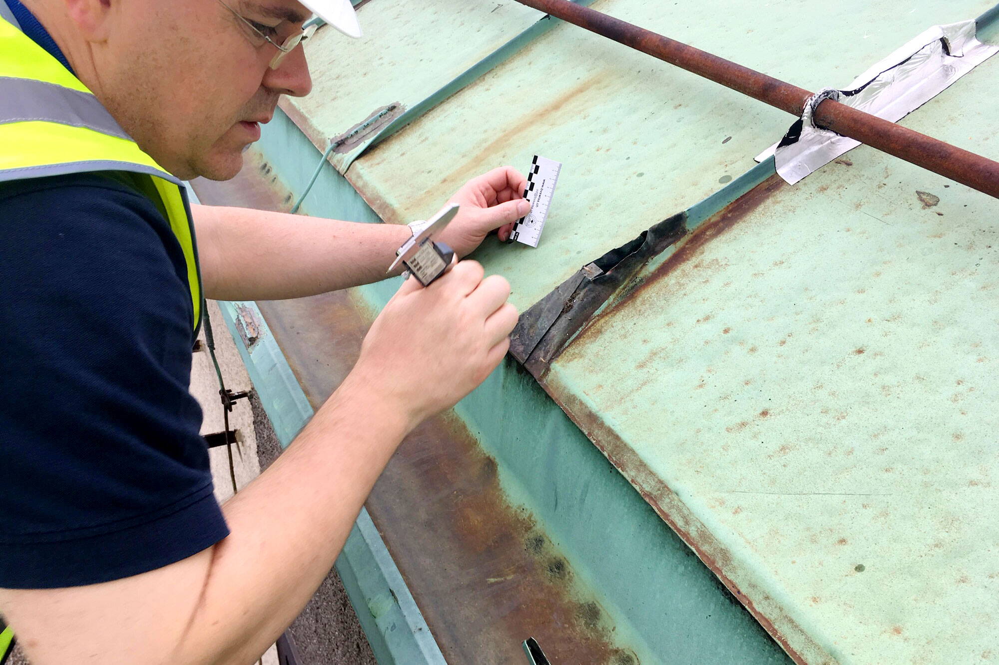 Ein Bauphysiker begutachtet und vermisst Schäden an einem einem Kupferdach.