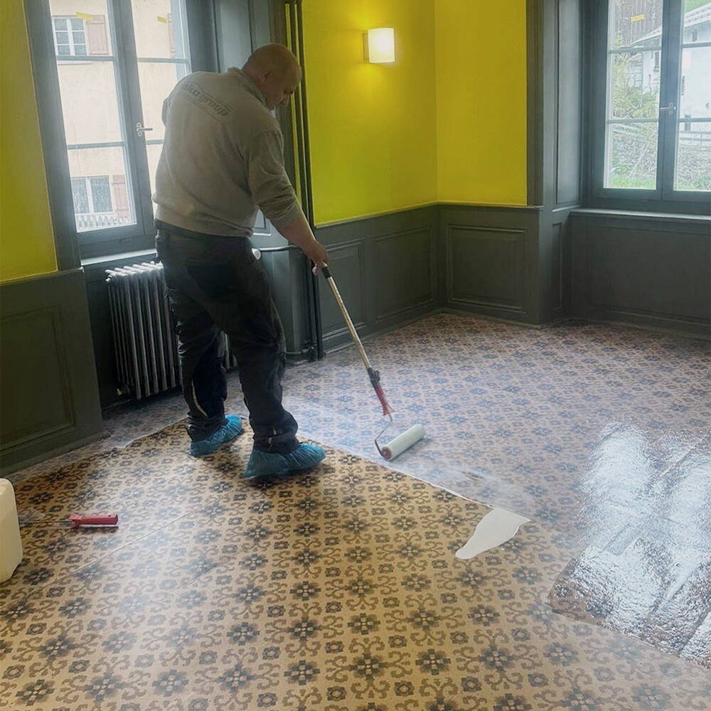 Der Mitarbeiter von akosan trägt auf den gemusterten, tiefengereinigten Linoleumboden eine Versiegelungsschicht auf.